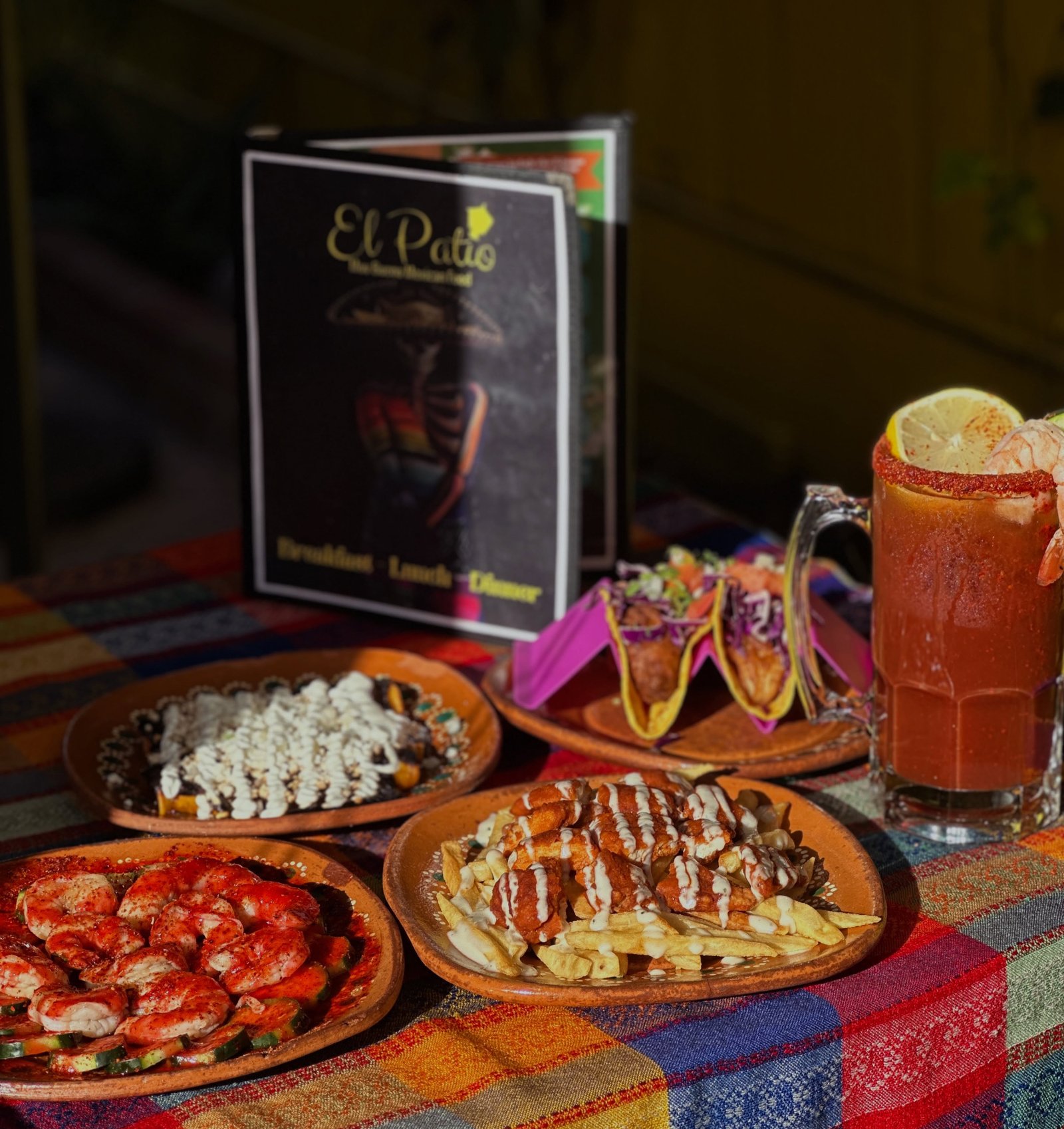 A spread of El Patio dishes — tacos, a shrimp plate, loaded fries and a michelada, with the El Patio menu