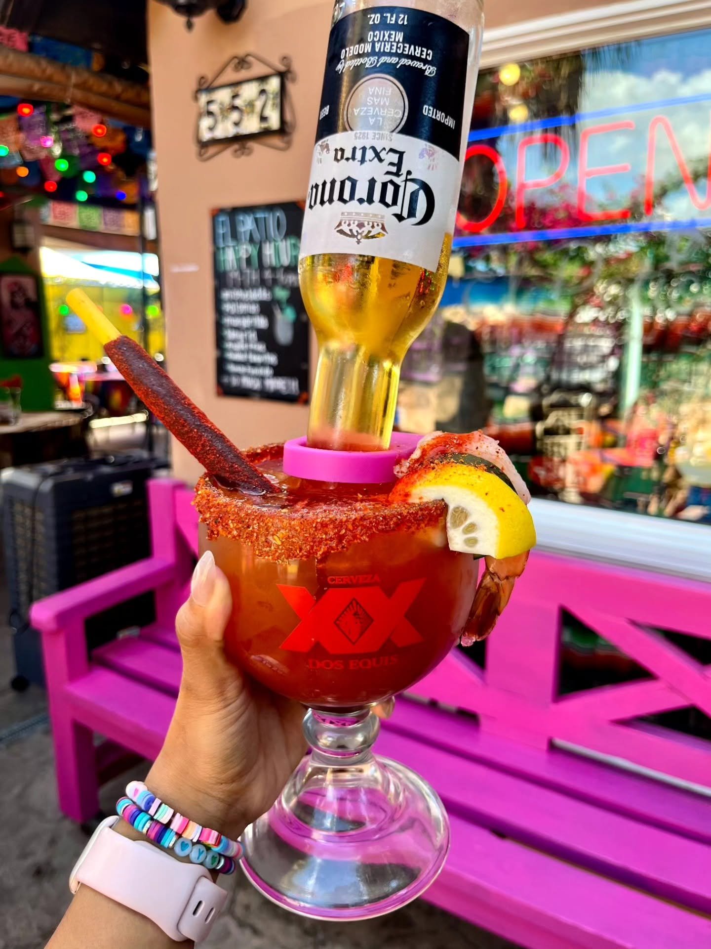 A michelada topped with a Corona in front of the pink bench