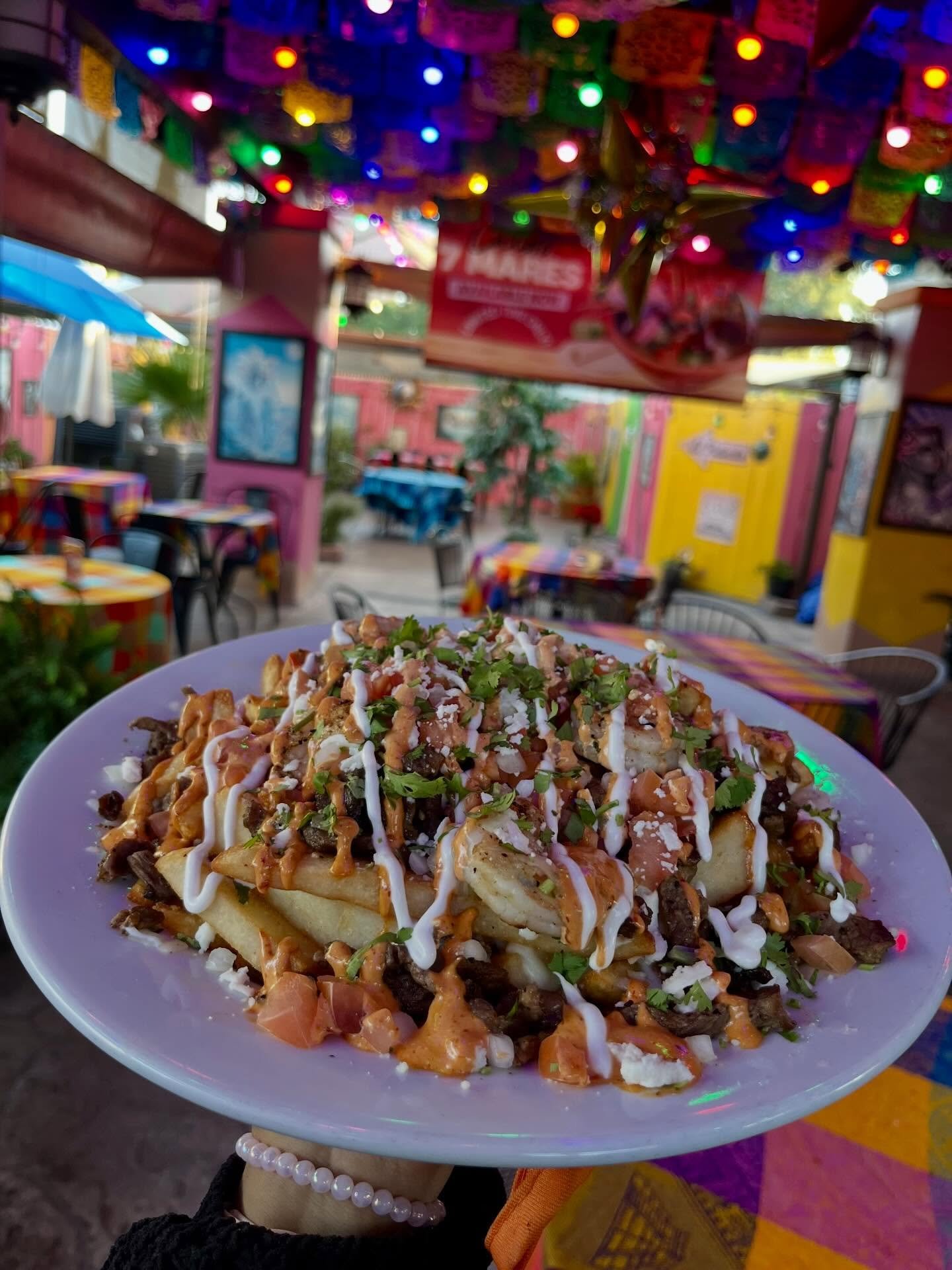 A loaded plate held up in front of El Patio's colorful papel-picado patio
